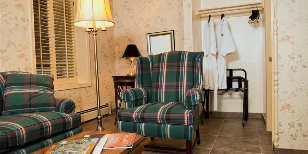 A room with a plaid sofa, a matching armchair, a floor lamp, and a small table with a magazine.