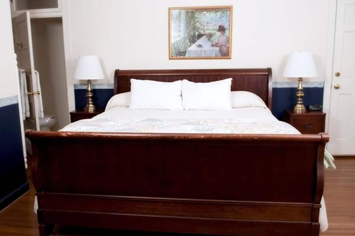 A neatly made bed with white linens, two bedside tables with lamps, a framed picture on the wall, and a door to the right.
