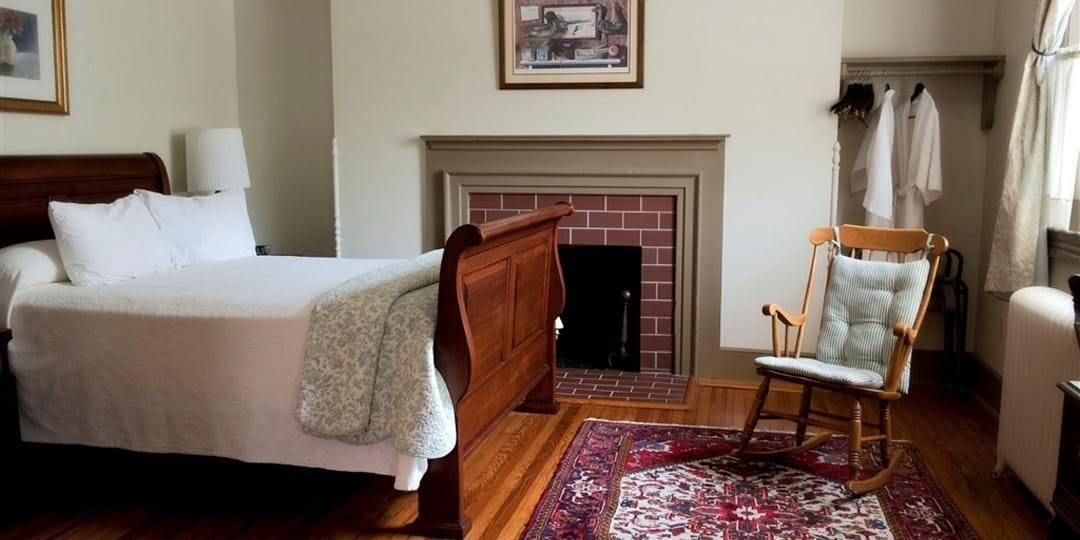 A bedroom with a bed, a rocking chair, a fireplace, and a patterned rug.