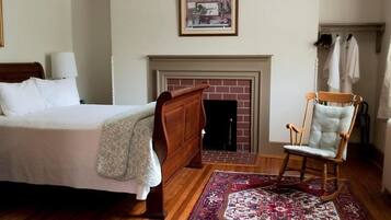 A bedroom with a bed, a rocking chair, a fireplace, and a patterned rug.