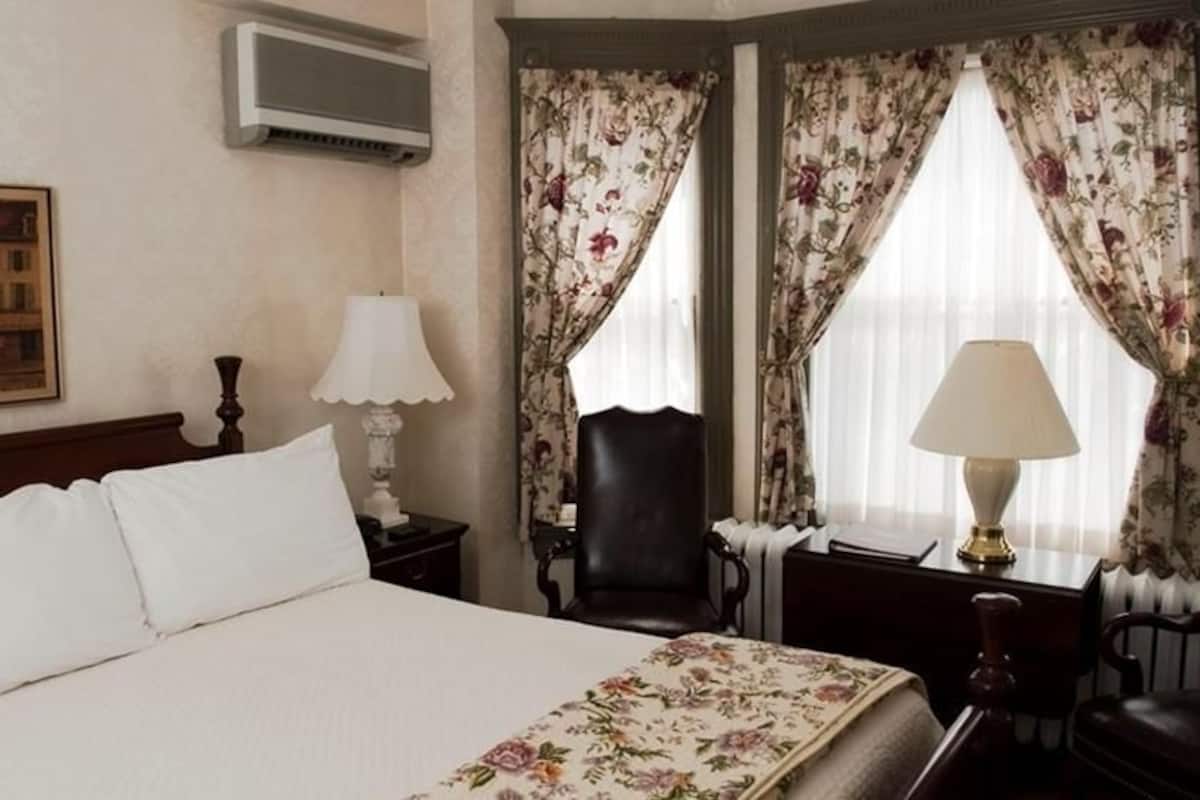 A hotel room with a large bed, two bedside tables with lamps, a chair, and a painting on the wall.