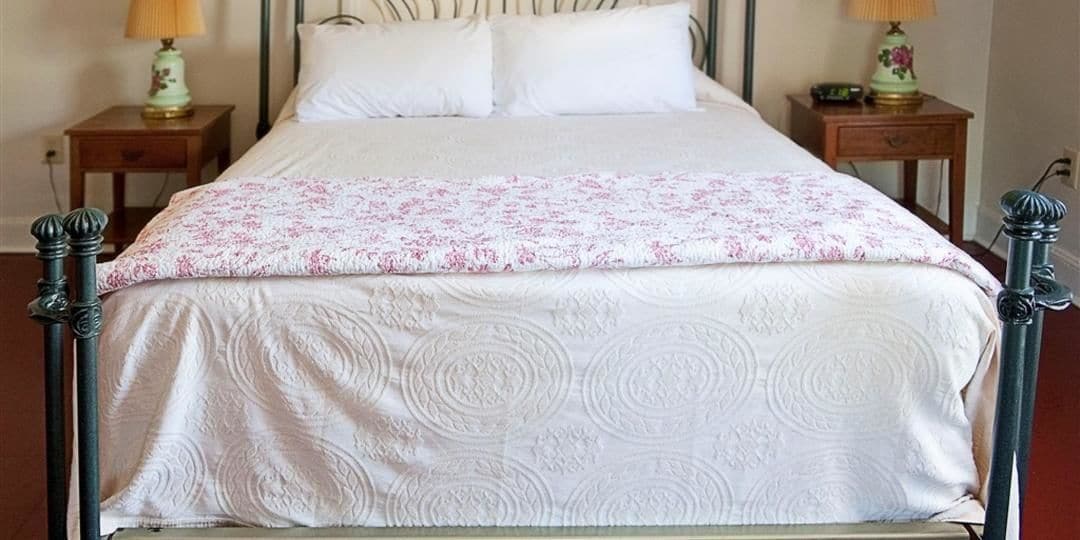 A neatly made bed with a floral-patterned bedspread and a white quilt. There are two bedside tables with lamps on either side of the bed.