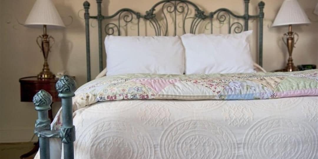 Ein ordentlich bezogenes Bett mit einer Blumensteppdecke, einem Metallkopfteil und zwei Nachttischlampen.