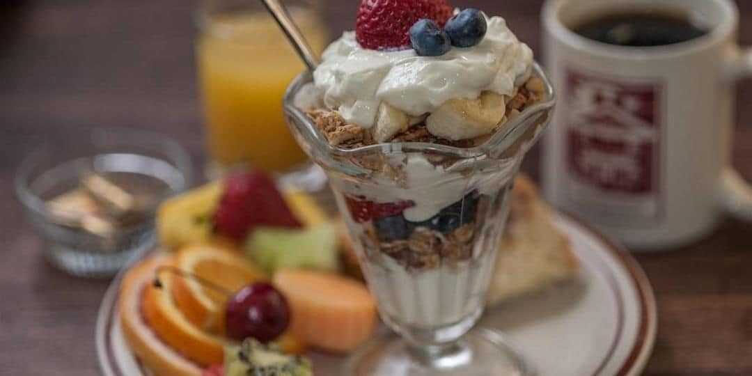 A breakfast setting with a layered dessert, a glass of orange juice, and a cup of coffee on a table.