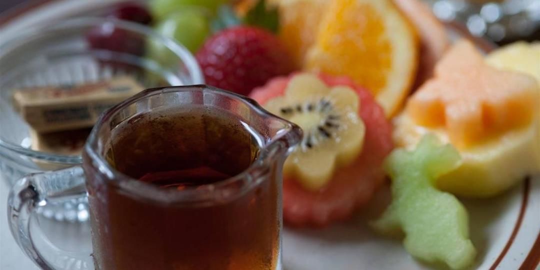 A glass pitcher of tea, a plate with sliced fruits, and a small dish with a chocolate bar.