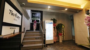 A reception area with a sign for 'Two Heart Hotel', a staircase, a refrigerator, and potted plants. - Two Heart Hotel (Daegu)