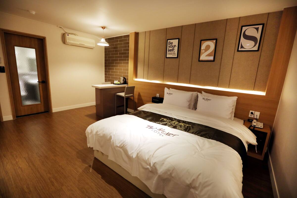 A hotel room with a bed, a desk, and a chair. There is a wall with a number '2' and a letter 'S' on it.