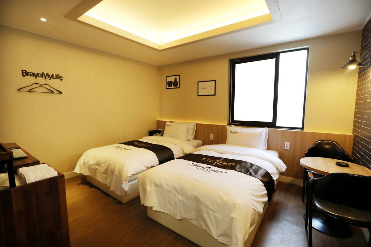 A hotel room with two beds, a desk, a chair, and a window.