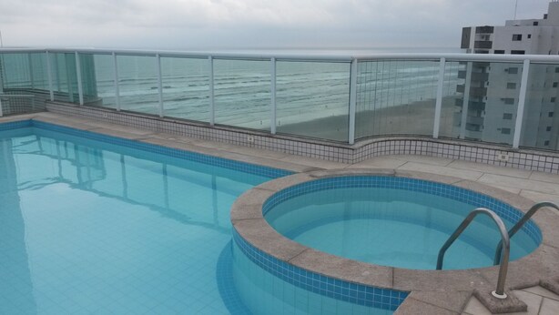 A swimming pool with a glass railing, a separate hot tub, and a view of the ocean. - Beachfront apartment (Praia Grande)