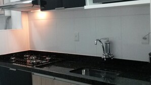 A modern kitchen with a black countertop, stainless steel appliances, and wooden cabinets. - Beachfront apartment (Praia Grande)