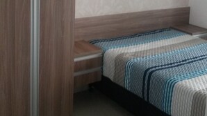 A bedroom with a bed, a wooden wardrobe, and a nightstand. - Beachfront apartment (Praia Grande)