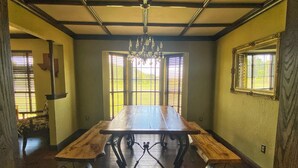 A dining room with a wooden table, metal legs, and a chandelier. There are windows with blinds and a mirror on the wall. - Multi-Family opportunity New Guest House ,Pool, Hot Tub,  Full camp Hook-ups, (Riesel)