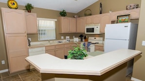 A kitchen with light wood cabinets, a central island, a microwave, a refrigerator, and a window with blinds. - Free Pool Heat, Free Wi-Fi, South Facing Pool and Privacy Fence (Kissimmee)