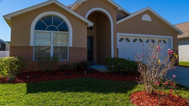 A single-story house with a beige exterior, a large arched window, and a garage. - Free Pool Heat, Free Wi-Fi, South Facing Pool and Privacy Fence (Kissimmee)