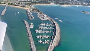 An aerial view of a coastal marina with boats docked, surrounded by a rocky breakwater and a small island. - Cosy 2 Bedroom Villa with super comfortable KING BEDS & luxury linen. Near Beach (Coffs Harbour)