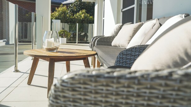 A wicker sofa with cushions, a wooden table with a glass vase, and a glass railing. - Cosy 2 Bedroom Villa with super comfortable KING BEDS & luxury linen. Near Beach (Coffs Harbour)