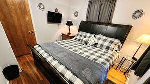 Une chambre à coucher avec un lit, une télévision, une lampe et un plancher en bois.