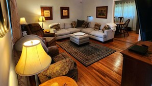Un salon comprenant un canapé, des fauteuils, une table basse, une lampe, un tapis et une table d’appoint en bois.