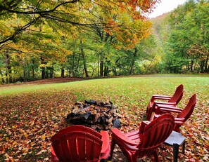 An outdoor seating area with a fire pit and red chairs, surrounded by trees with autumn leaves.