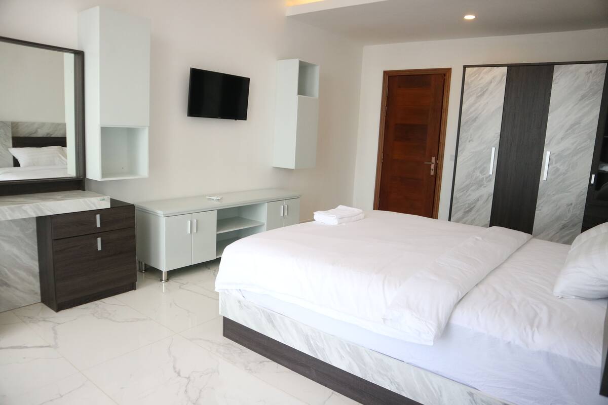 Een moderne hotelkamer met een groot bed, een ingebouwde televisie, een kledingkast en een kaptafel met spiegel.