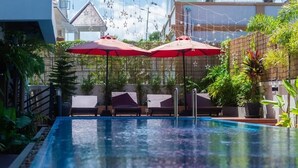 Ein Pool im Freien mit Liegestühlen und roten Sonnenschirmen, umgeben von viel Grün und einem Bambuszaun.