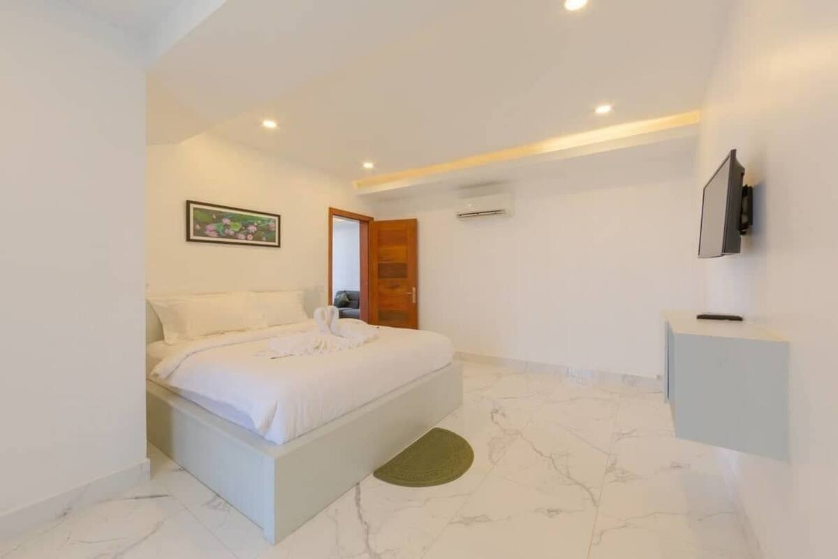 Een moderne slaapkamer met een bed, een schilderij, een televisie en een airconditioner.