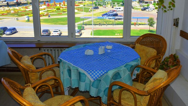 A room with a view of the sea, a table with a checkered tablecloth, wicker chairs, and a window with a view of a parking lot and a road. - Hotel Ülke (Yalova)