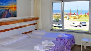 A hotel room with two beds, a window with a view of a parking lot and a garden, and a painting on the wall. - Hotel Ülke (Yalova)