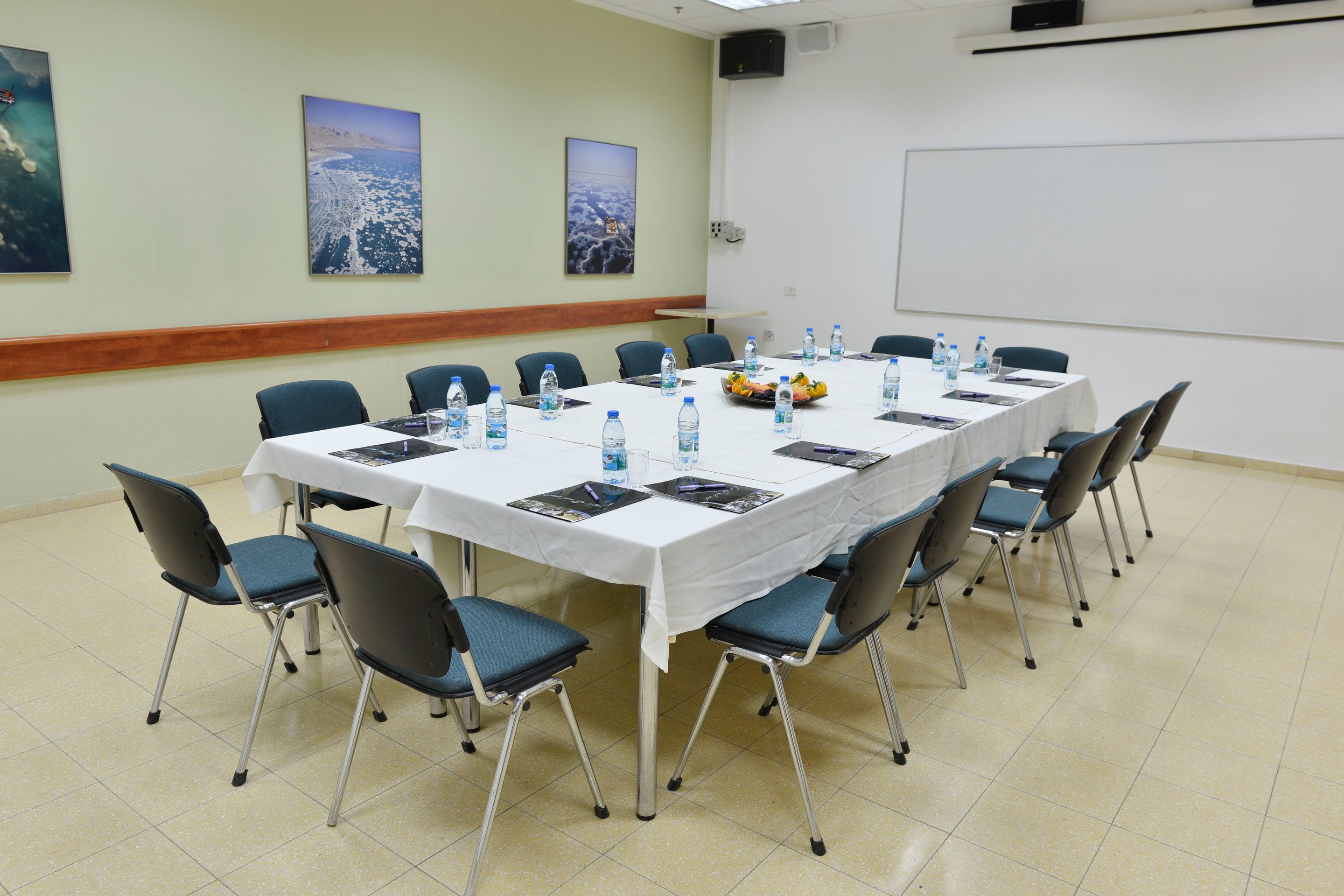 A conference room with a long table, chairs, water bottles, and a projector screen.