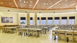 A large conference room with multiple tables and chairs, large windows with blinds, and a high ceiling with a grid pattern. - HI Masada Hostel (Tamar)