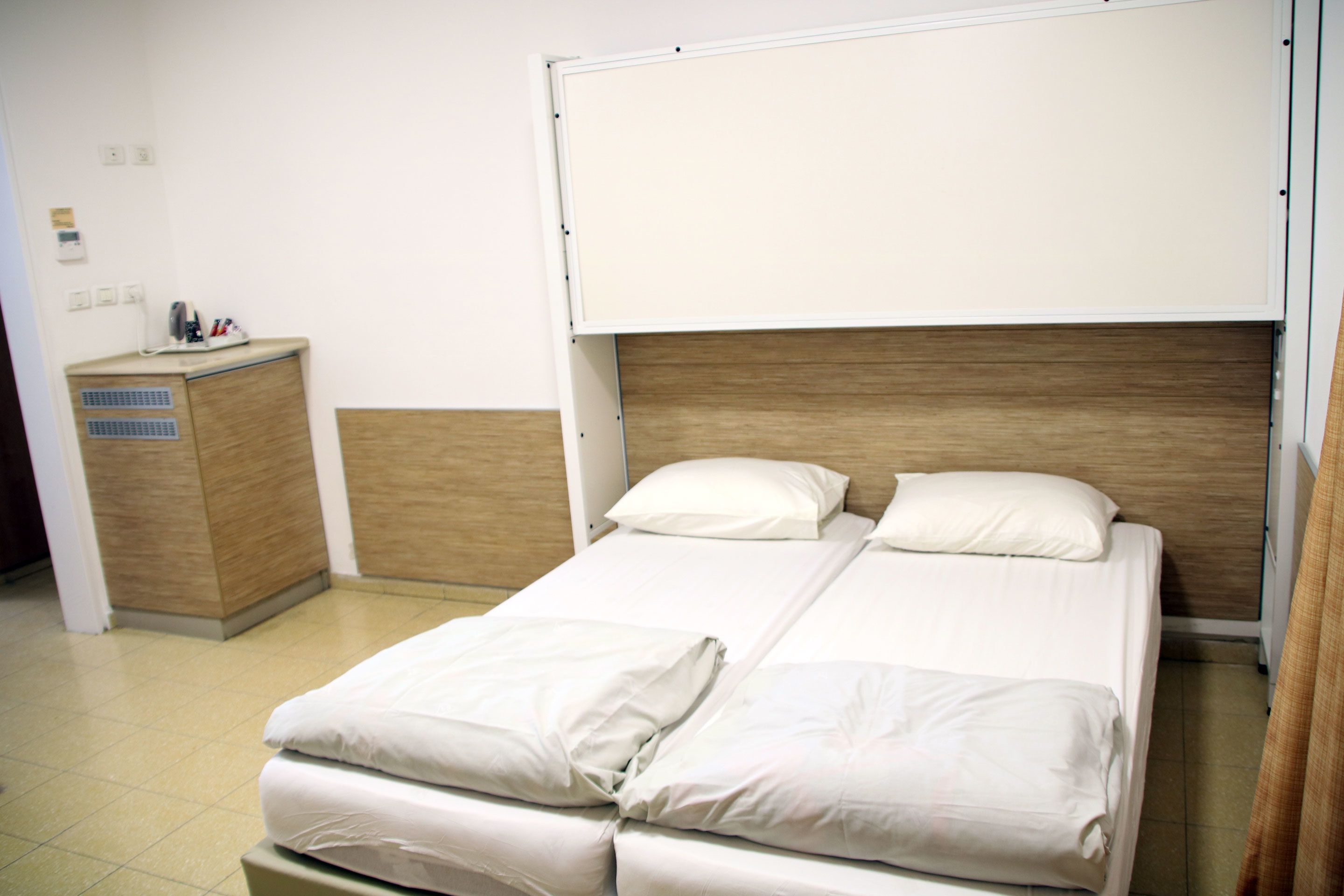 A hotel room with a bed, a wooden headboard, a bedside table, and a small cabinet.
