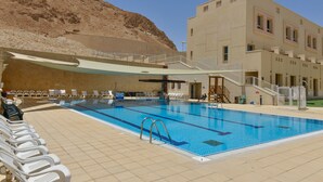 A swimming pool with a view of a desert landscape, a covered seating area, and a building with multiple windows. - HI Masada Hostel (Tamar)