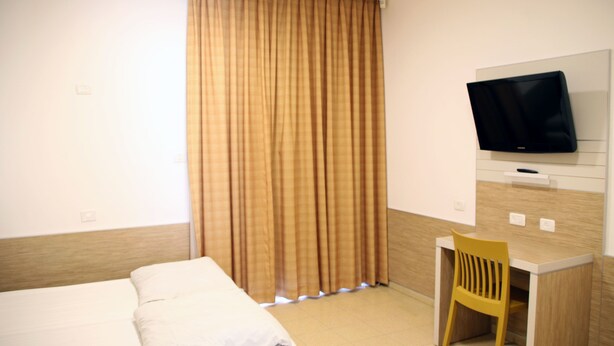 A hotel room with a bed, a desk, a chair, and a TV mounted on the wall. - HI Masada Hostel (Tamar)
