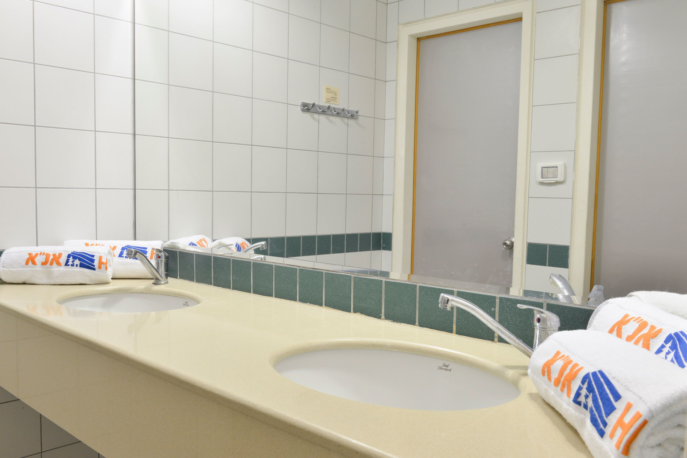 A bathroom with two sinks, a mirror, and towels with a logo.