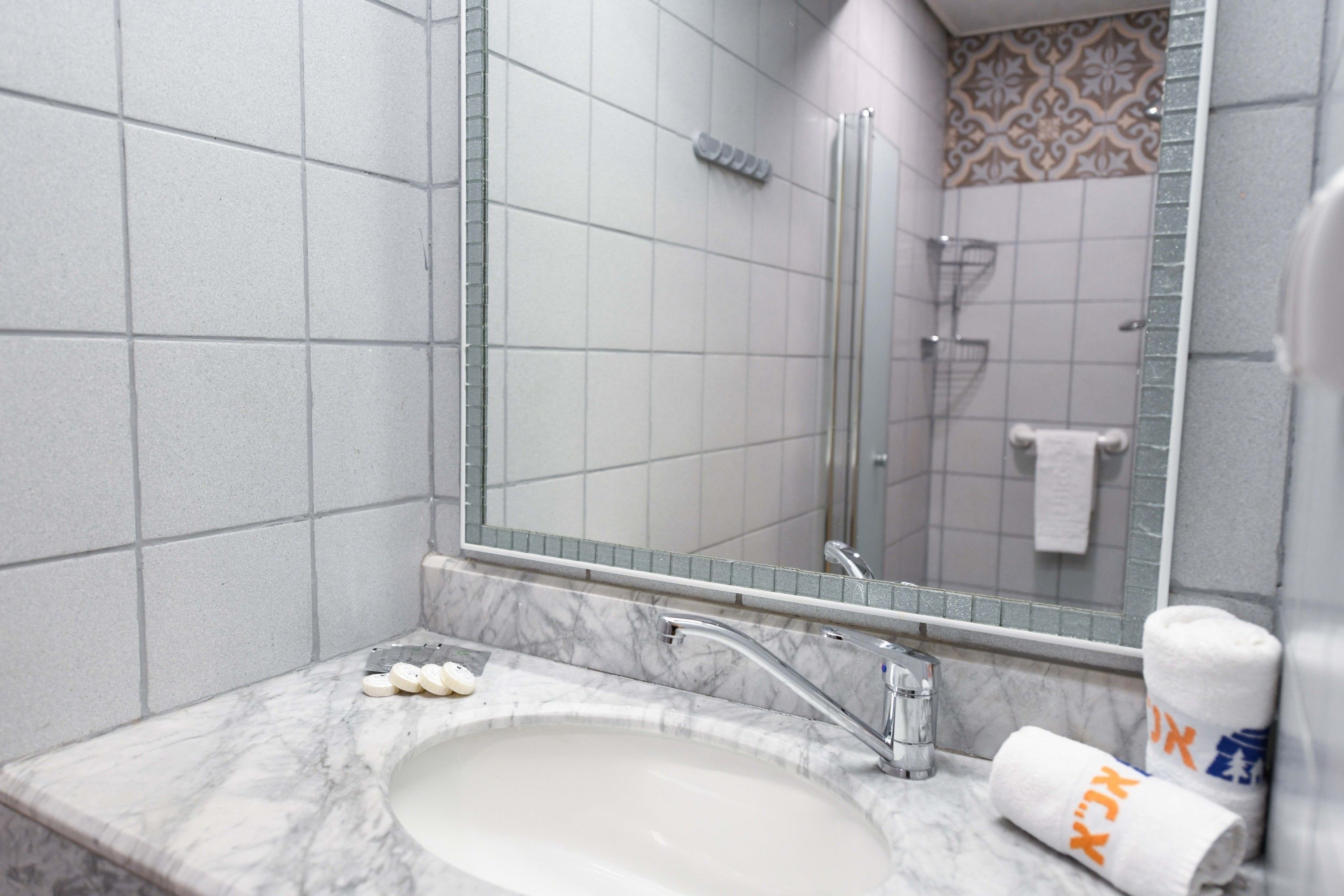 Un baño con lavamanos de mármol, cabina de ducha con mampara de vidrio y un espejo que refleja la zona de la ducha.