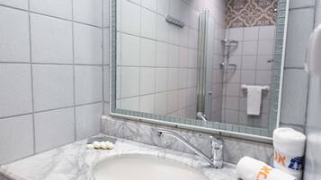 Un baño con lavamanos de mármol, cabina de ducha con mampara de vidrio y un espejo que refleja la zona de la ducha.
