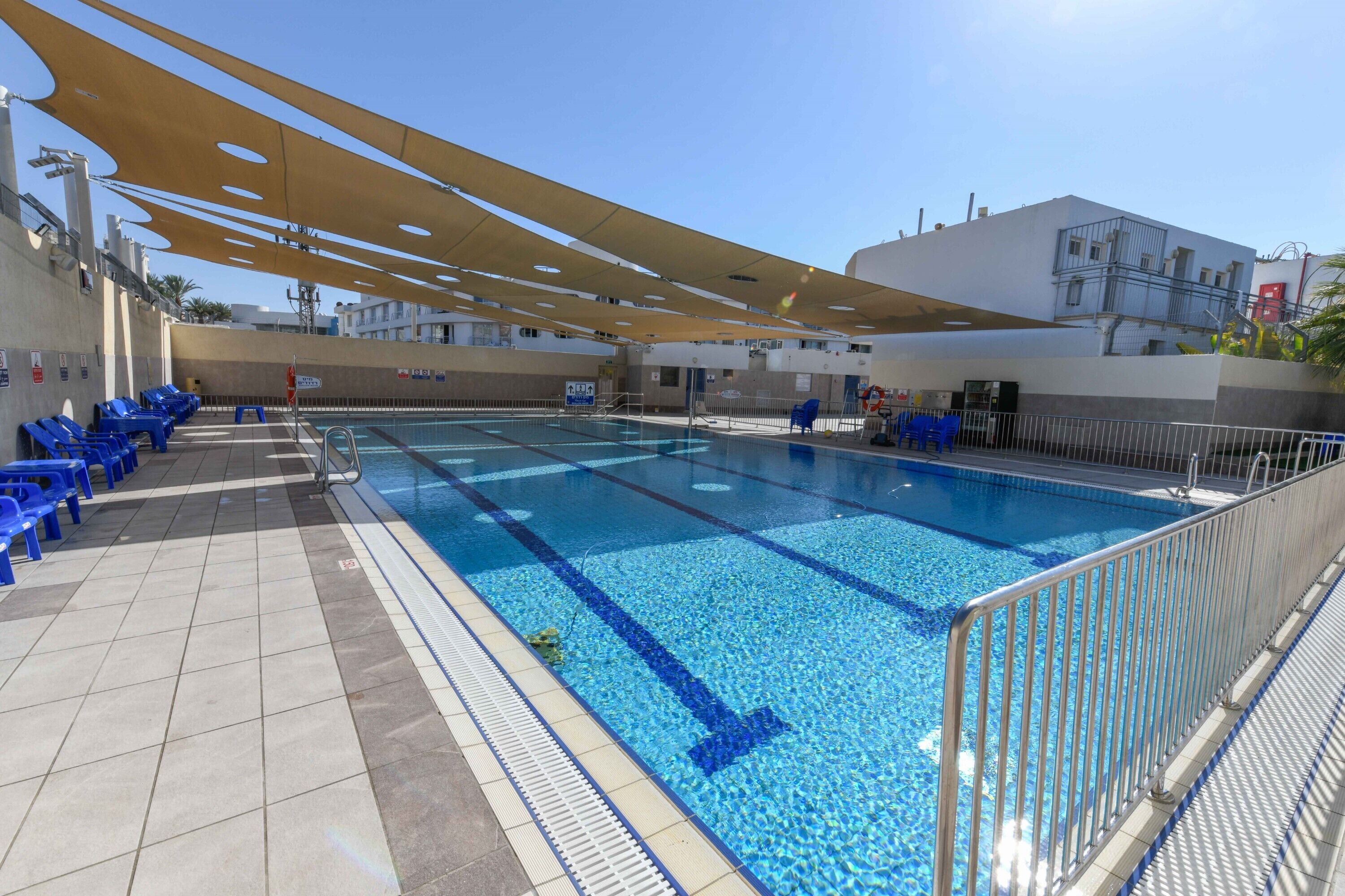 A swimming pool with blue tiles, a sunshade, and blue chairs along the side.
