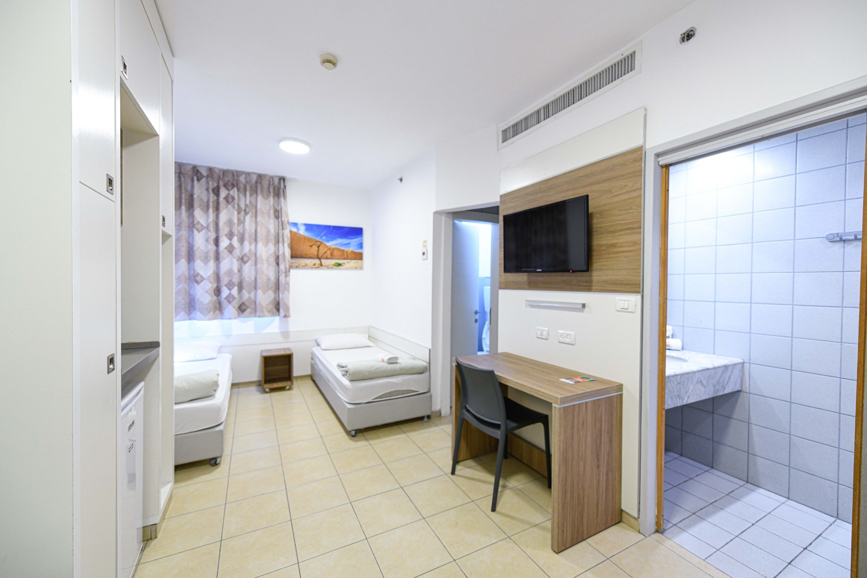 A modern hotel room with a bed, a desk, a TV, and a bathroom.