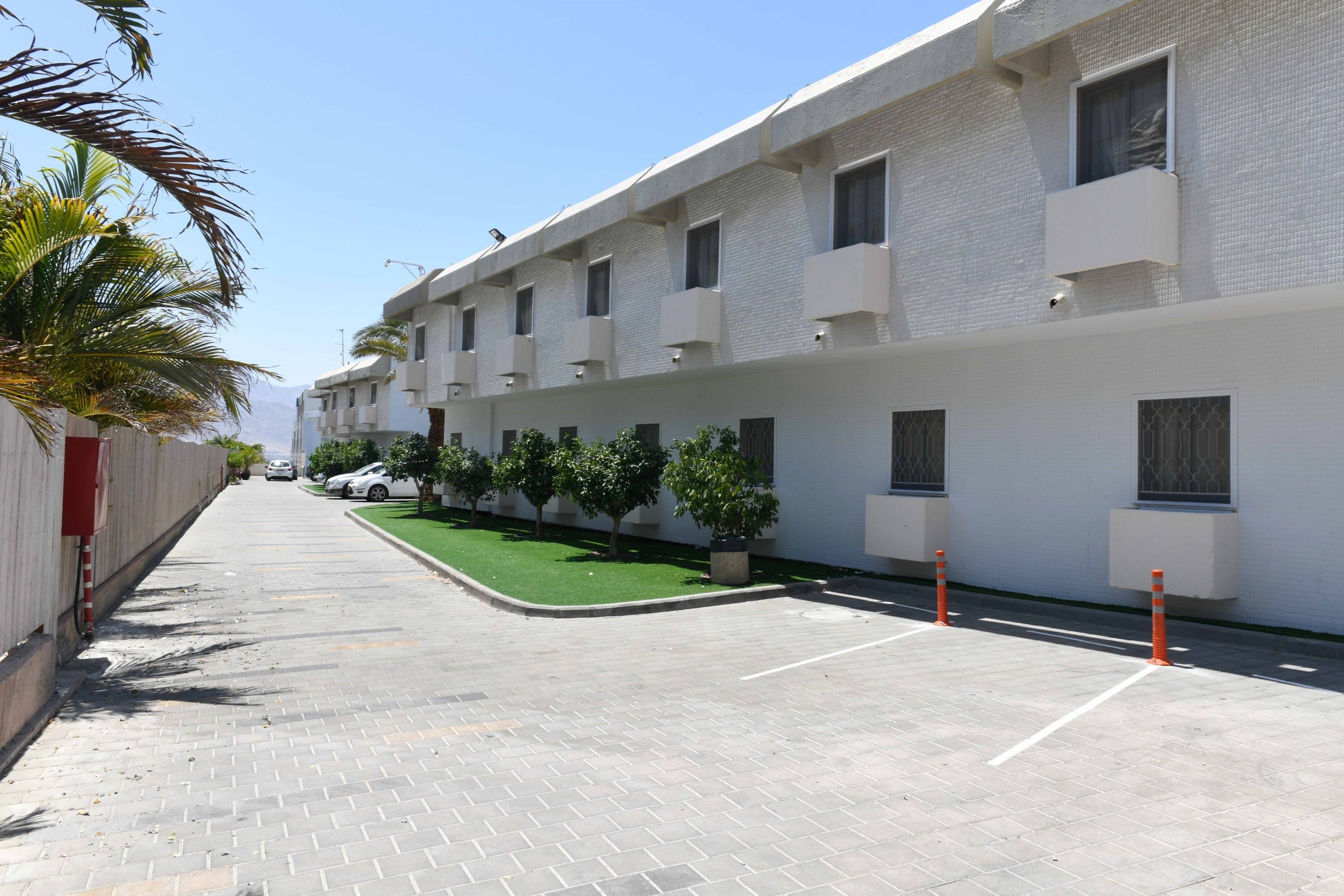 A multi-story building with a clean, modern design, featuring balconies and a paved walkway.