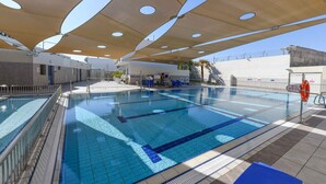 A swimming pool with clear blue water, surrounded by a tiled deck and shaded by large overhead canopies. - HI Eilat Hostel (Eilat)