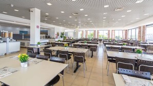 A spacious cafeteria with multiple tables and chairs, a ceiling with a grid pattern, and large windows allowing natural light. - HI Eilat Hostel (Eilat)