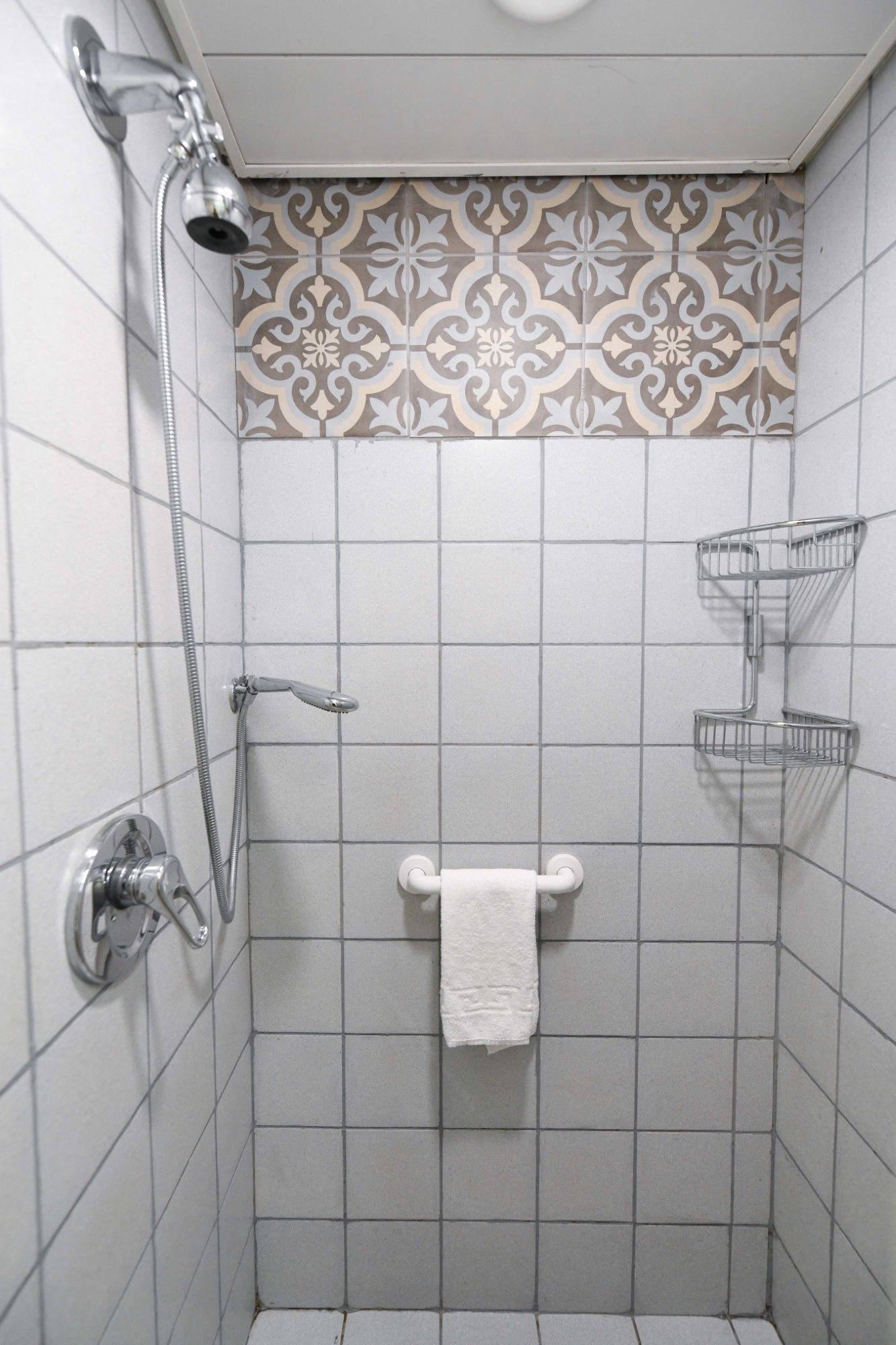 A shower with a handheld showerhead, a towel rack, and a shower caddy.