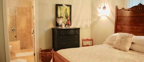 Un dormitorio con cama, cómoda, silla, lámpara de pared y puerta que da al baño.