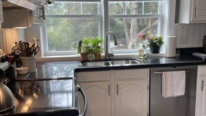Una cocina moderna con armarios blancos, un lavamanos de acero inoxidable y una ventana con vistas a árboles.