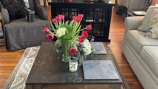 Una sala de estar con una mesa de centro de madera oscura, un jarrón con flores rojas y blancas, y un sofá gris.