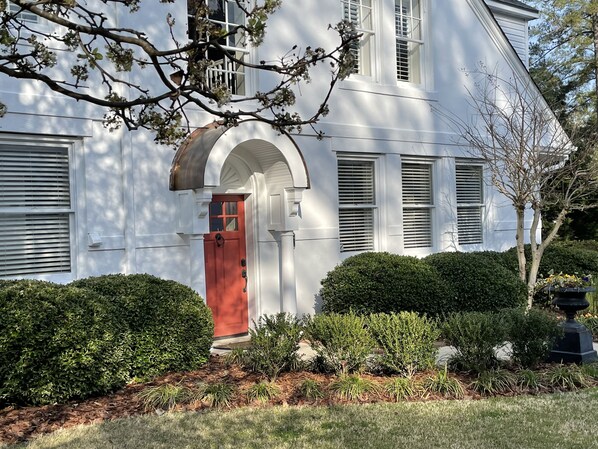 Ein weißes Haus mit roter Tür, weißen Fensterläden und einem gepflegten Garten.