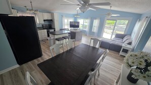 Une cuisine moderne avec un coin repas, un réfrigérateur noir, des meubles blancs et un ventilateur de plafond.