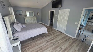 Une chambre à coucher comprenant un lit, une commode, un ventilateur de plafond et un téléviseur fixé au mur.