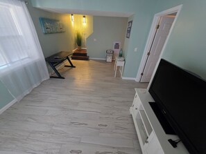 A living room with a flat-screen TV, a coffee table, a bench, a potted plant, and a staircase leading to another level.