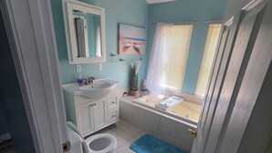 Une salle de bain équipée de toilettes, d’un lavabo et d’une baignoire, avec un mur bleu et des accessoires blancs.